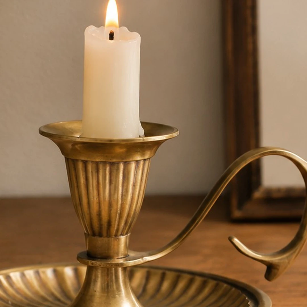 Lit candle seated inside the Aura brass candlestick cup