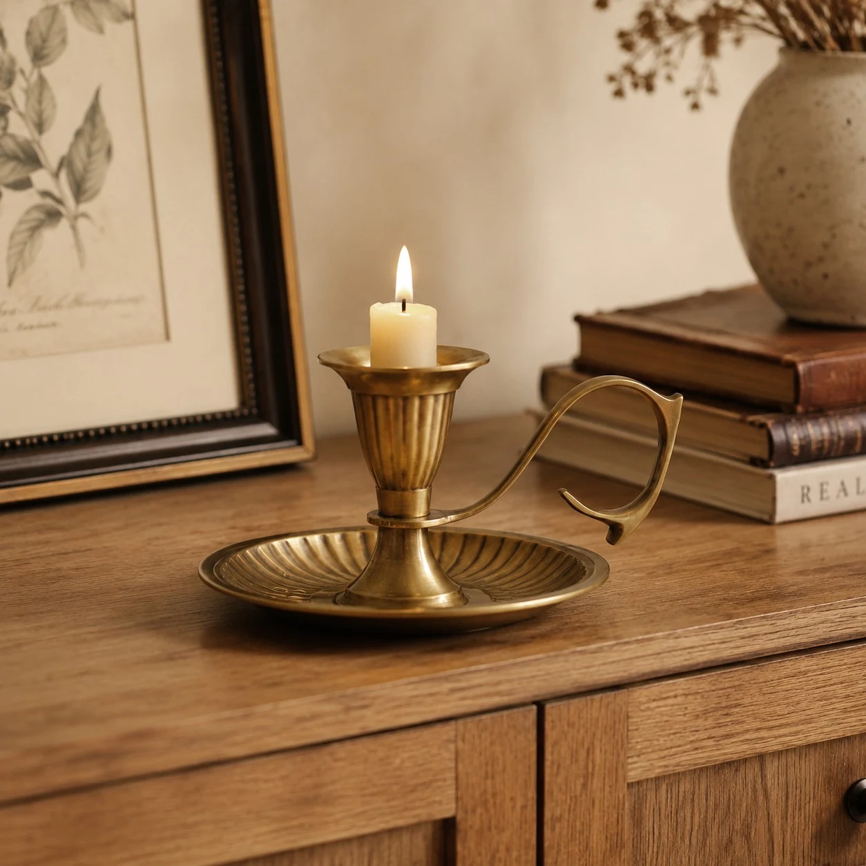 Aura brass candlestick with a lit candle on a wooden cabinet